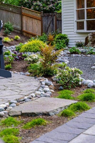 Stone paver garden pathway with river rock border and mixed plantings alongside residential home